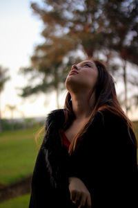 Thoughtful young woman in warm clothing looking up while standing at park