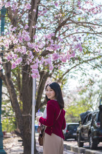 Rear view portrait of woman standing by pink flowering tree