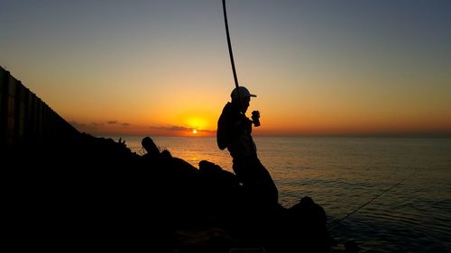 Silhouette man fishing at sea against sky during sunset