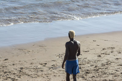 Rear view of shirtless man standing on beach