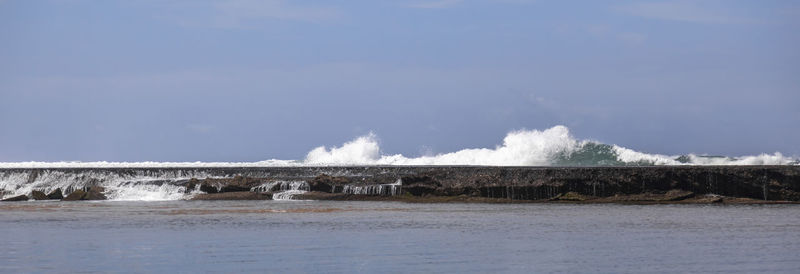 Panoramic shot of sea waves splashing on shore against sky