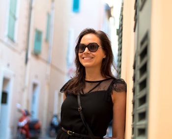 Smiling young woman standing against building