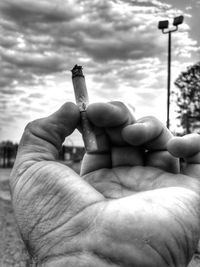 Close-up of hand holding cigarette against sky