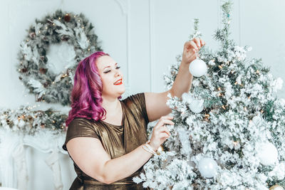 Smiling woman decorating christmas tree at home