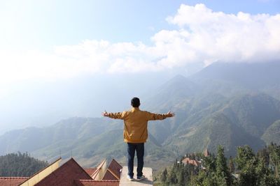 Rear view of man standing on mountain against sky