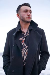 Young man looking away while standing against sea