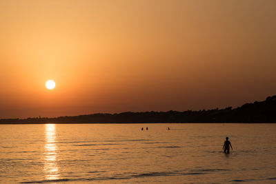 Silhouette woman in sea against orange sky during sunset