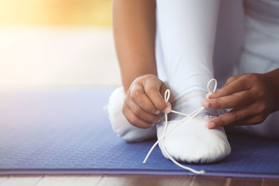 Low section of woman wearing shoe while sitting on floor