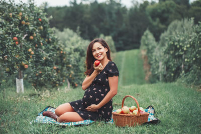 Young woman sitting in basket on field against trees