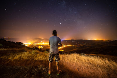 Rear view of man standing on field against sky at night