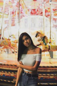 Portrait of young woman standing illuminated amusement park ride at night