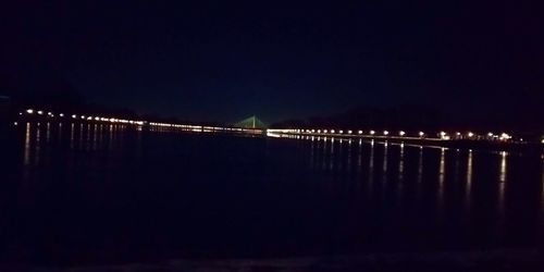 Illuminated bridge over silhouette water against clear sky at night