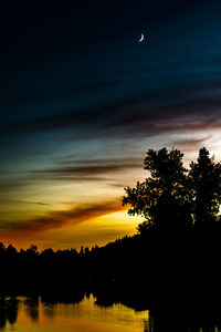 Silhouette trees by lake against sky during sunset