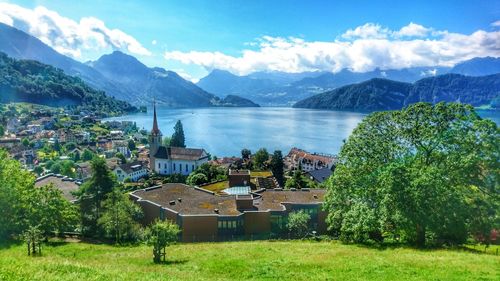 Scenic view of houses by lake and mountains against cloudy sky