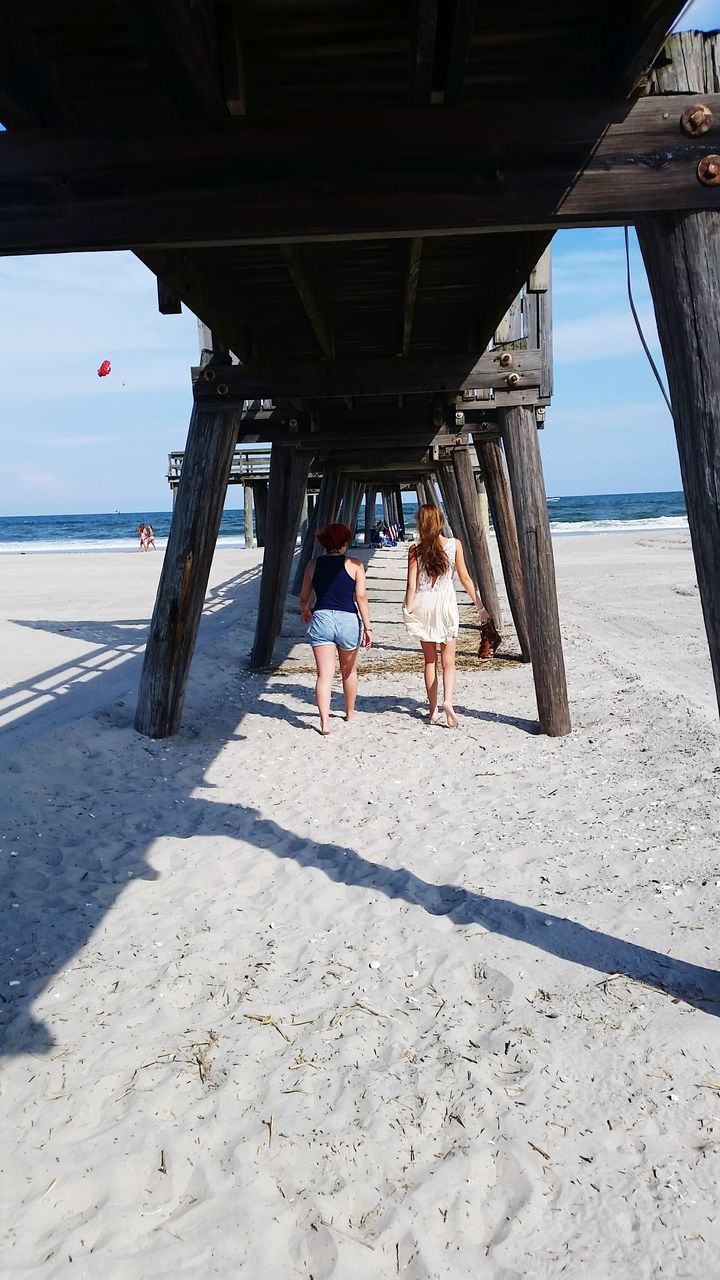 beach, sea, horizon over water, sand, shore, water, lifestyles, leisure activity, sky, built structure, full length, vacations, person, pier, rear view, architecture, sunlight, day