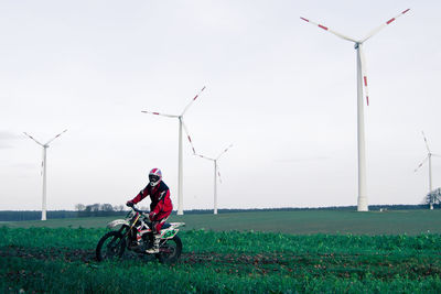 Person riding motocross by windmills on field against sky