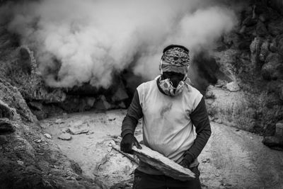 Man wearing gas mask holding rock outdoors