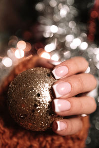 Female hand with french manicure holding a gold christmas ball. winter holiday celebration. new year