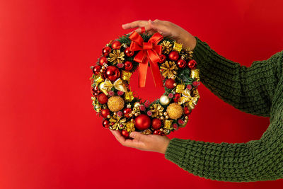 Minimalistic festive design, christmas decorative wreath in female hands on red background