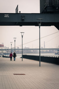 People walking beside river against clear sky