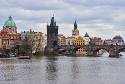 Bridge over river by buildings against sky in city