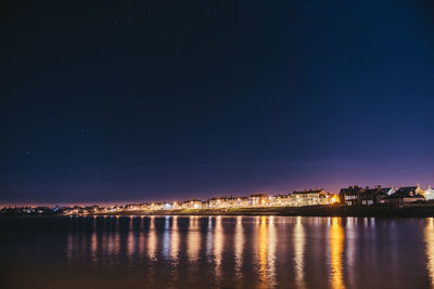 Illuminated houses by river against sky at night