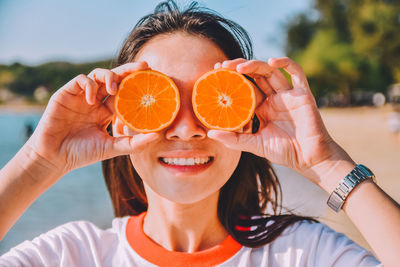 Close-up of smiling woman holding orange fruit at beach