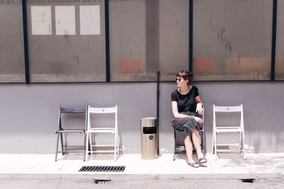 Young woman sitting on chair at sidewalk