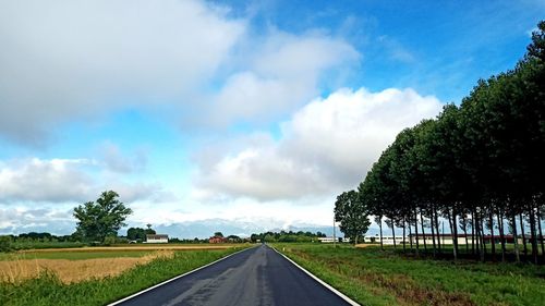 Empty road amidst trees on field against sky