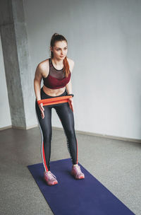 Full length of young woman exercising against wall