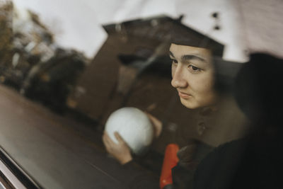 Teenage boy with soccer ball day dreaming seen through car window