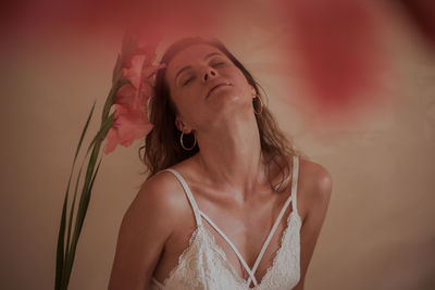 Young woman with eyes closed sitting against wall at home