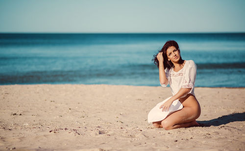 Portrait of seductive woman kneeling at beach during sunny day