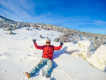 Portrait of man showing thumbs up while sitting on snowcapped mountain against sky