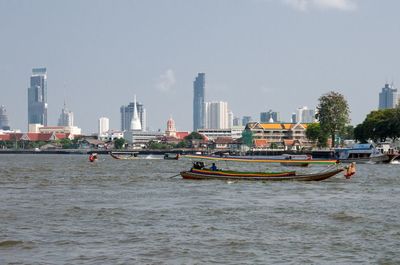 Boats in river by buildings in city against sky