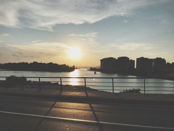 Silhouette buildings by river against sky during sunset