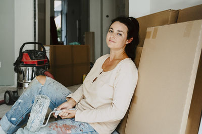 Portrait of smiling woman sitting by cardboard during home renovation