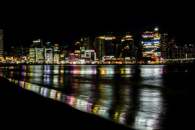 Illuminated buildings by sea against sky at night