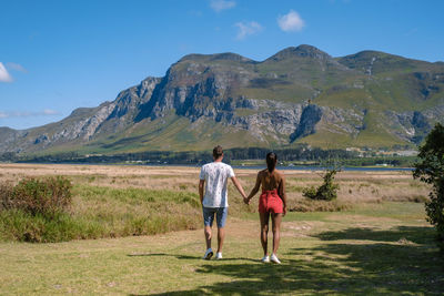 Rear view of couple walking on field against mountain