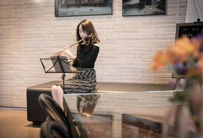 Woman playing musical instrument while sitting against wall