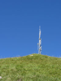 Low angle view of telephone pole on field against clear blue sky