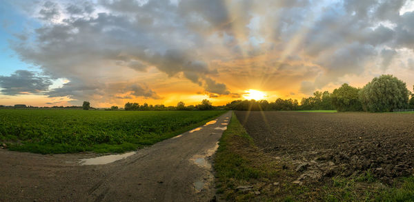 Road amidst field against sky during sunset