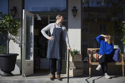 Colleague looking at male owner while shielding eyes outside store on sunny day