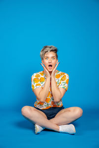 Portrait of young woman sitting against blue background