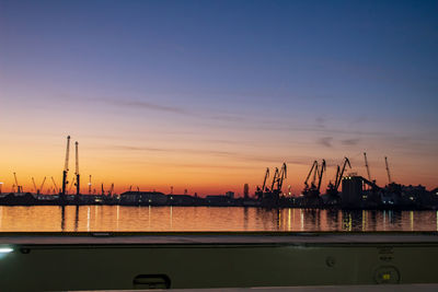 Cranes at commercial dock against sky during sunset