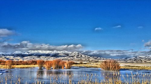 Scenic view of lake and snowcapped mountains against blue sky