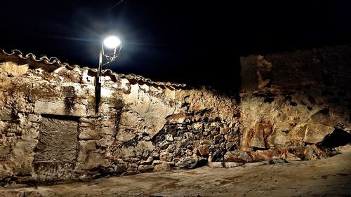 Low angle view of illuminated street light against wall at night