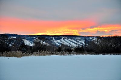 Snow covered landscape against sky during sunset