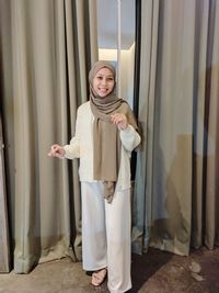 Portrait of smiling woman standing against curtain