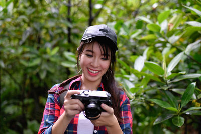 Smiling woman photographing while standing against plants